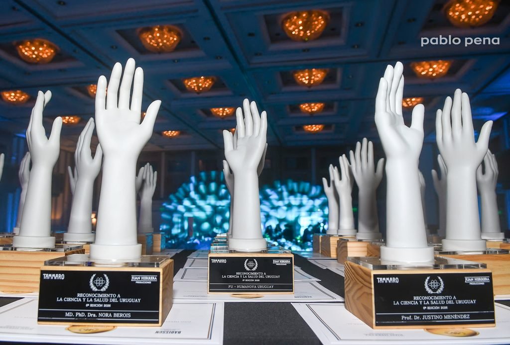 Estatuillas en forma de mano del Reconocimiento a la Ciencia y la Salud del Uruguay sobre la mesa, con placas de los homenajeados, en el Radisson Montevideo Victoria Plaza Hotel